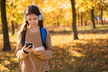 Girl with phone and power bank in hands in autumn park. Young beautiful student with a phone and charging in his hand search music using mobile app