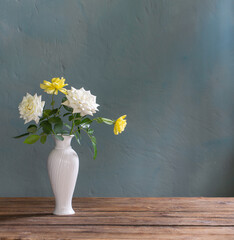  roses in white vase on wooden table on background dark wall