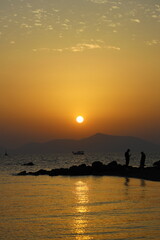 two people talking by the sea at sunset and a lonely fishing boat in the sea