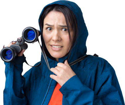 A tourist girl in a blue raincoat holds binoculars in her hands and looks into the distance, spies.