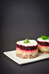 Side view of Scandinavian layered fish salad Herring under fur coat. Portion with marinated herring, onion, grated potato, beetroot, mayonnaise on top. Dark copy space background