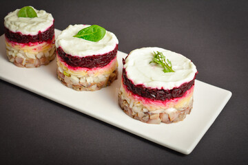 Top view of Norwegian layered fish salad Herring under fur coat. Portion with marinated herring, onion, grated potato, beetroot, mayonnaise on top with lettuce olive salad. Dark copy space background