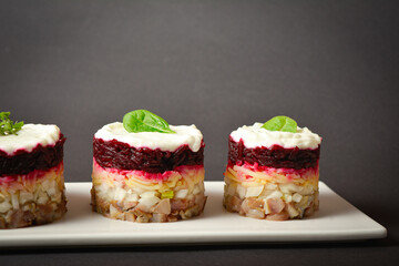 Side view of Traditional holiday layered fish salad Herring under fur coat served in culinary rings. Three serving sizes of Eastern Europe salad with beetroot, potato, onion, fish and mayonnaise