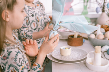 easter holiday time in spring season. happy family candid little kids sisters girls have fun at home decorating table with eggs in napkin like ears rabbit. traditional food. festive home decor