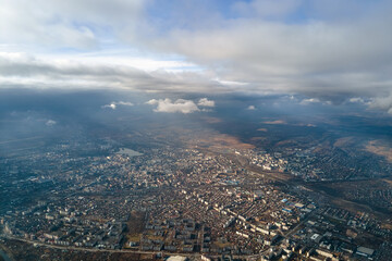 Aerial view from high altitude of distant city covered with puffy cumulus clouds flying by before...