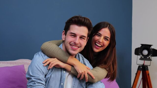 Close up portrait of happy caucasian young couple hugging and smiling together in a couch at home. Beautiful brunette wife embracing her husband resting in a sofa indoors. High quality photo