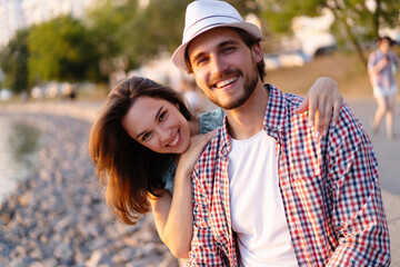 Fototapeta na wymiar Happy young couple in love. Pretty girl cuddling with boyfriend on beach and bright warm lens flare.