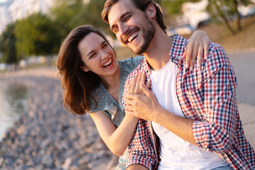 Happy young couple in love. Pretty girl cuddling with boyfriend on beach and bright warm lens flare.