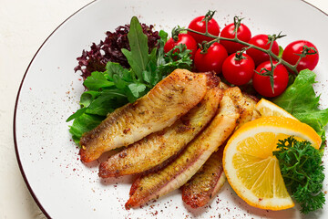Fried Tilapia fish fillet, in spices, with cherry and salad, on a white plate, homemade, no people,