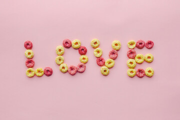 Creative word love making with colorful corn flakes on pink background