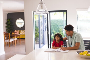 Hispanic father sitting beside blind son reading book with braille in kitchen at home