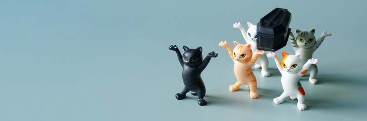 Toy dancing kittens with raised paws amusingly carry a black coffin. Concept of a funeral procession dancing with a coffin. Social advertising of the need to monitor your health. Web banner. - obrazy, fototapety, plakaty