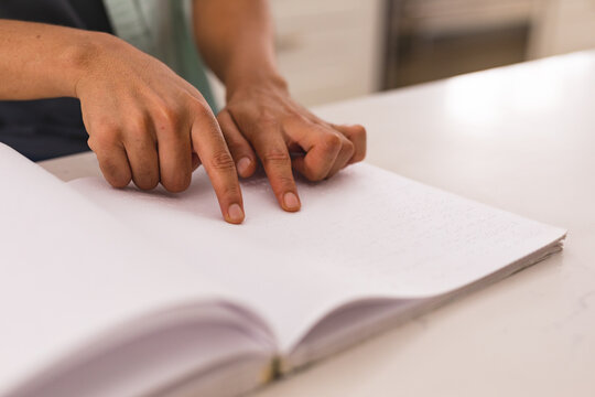 Cropped hands of blind hispanic man touching braille on book while reading at home