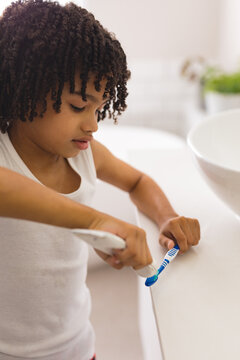 Hispanic curly haired boy removing toothpaste on toothbrush in bathroom at home