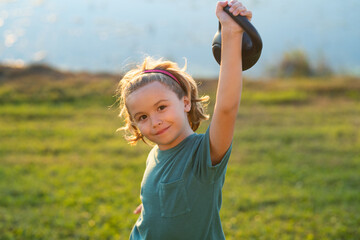 Sport child workout. Child exercising with kettlebell. Sporty child with dumbbell. Fit kids training. Child lifting the kettlebell in backyard outside.