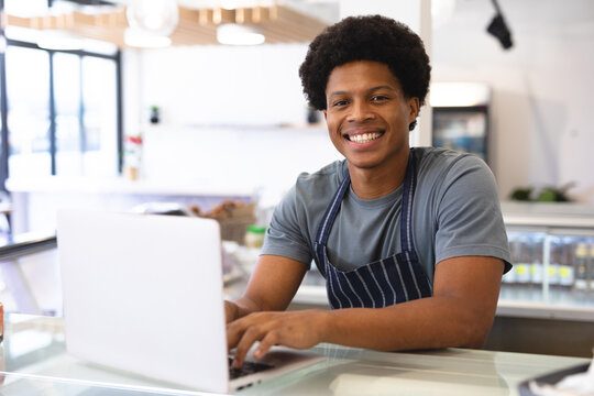 Portrait of smiling young african american owner sitting with laptop at counter in coffee shop