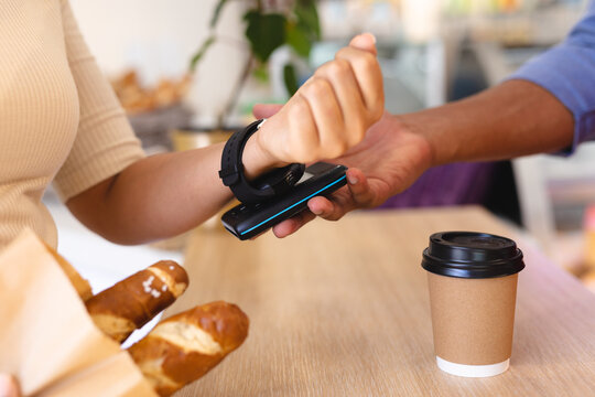 Female caucasian customer paying through digital wallet from smartwatch at counter in coffee shop
