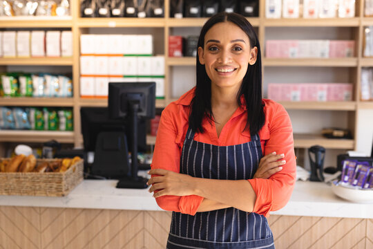 Portrait of smiling confident young female owner with arms crossed wearing apron at coffee shop