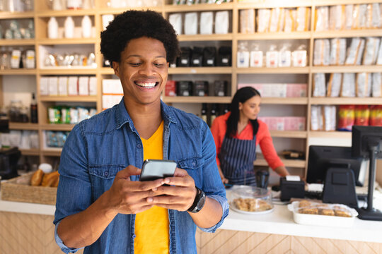 Smiling young african american male customer using smartphone against owner at coffee shop