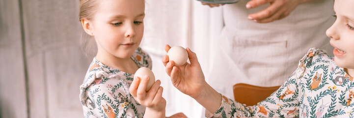 easter holiday time in spring season. happy family candid little kids sisters girls and mother mom have fun at home, traditional shackling, jarping or dumping with eggs. religious tradition. banner