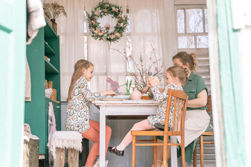 easter holiday time in spring season. happy family candid little kids sisters girls together mother have fun at home decorating table for lunch or dinner. traditional food. festive home decor
