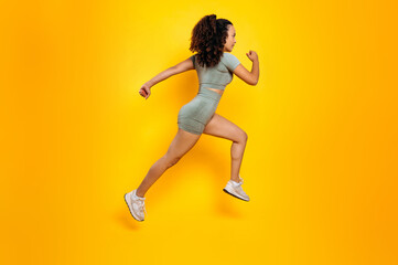 Fototapeta na wymiar Workout concept. Sports lifestyle. Full length side view photo of a fitness, sporty, motivated mixed race woman in sportswear, training working out, jumping, running, isolated yellow background