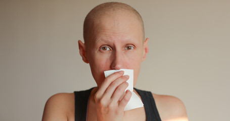 Bald cancer sick woman blowing running nose got flu cough cold, rhinitis sneezing in tissue or nosebleeds. Female is sick allergic having allergy symptoms coughing holding napkin. Misery, infelicity