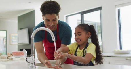 Happy biracial father and daughter washing hands in kitchen