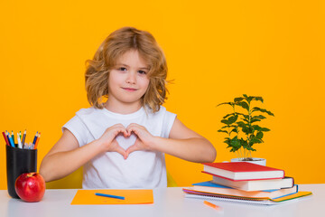 Pupil with love heard sign. Nerd pupil boy from elementary school with book isolated on yellow studio background. Smart genius intelligence kid ready to learn. Back to school.