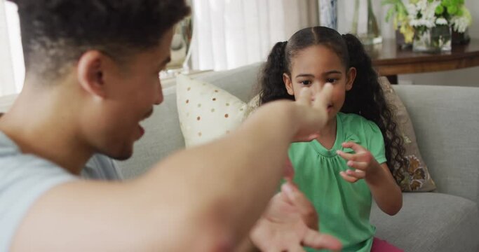 Happy biracial father and daughter sitting on sofa using sign language