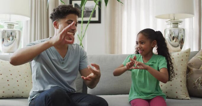 Happy biracial father and daughter sitting on sofa using sign language