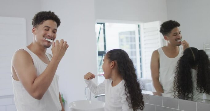 Happy biracial father and daughter washing teeth in bathroom together
