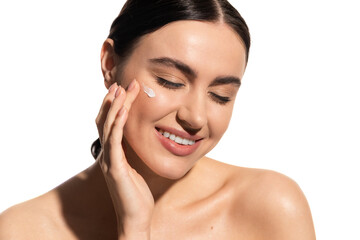 satisfied young woman applying moisturizing face cream on cheek isolated on white.