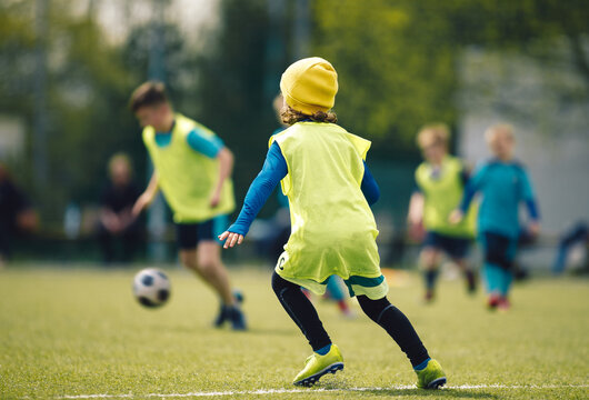 Children play football during winter soccer tournament. Kids play soccer at grass field. Young boy in winter cap play soccer with friends on sunny winter day