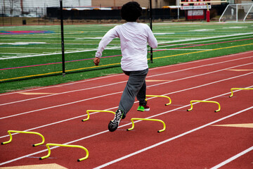 Rear view of a boy running fast over small hurdles on a track