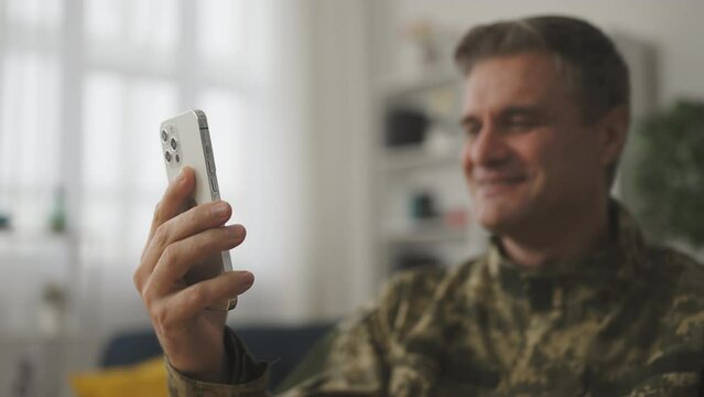 Closeup of smiling middle-aged male soldier having video call on smartphone
