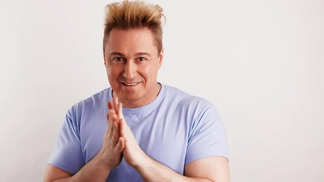 European man rubbing his hands thinking over choice, planning evil tricky prank or scheming. Smiling handsome guy pondering idea, wears blue t-shirt. Indoor studio shot isolated on white background.