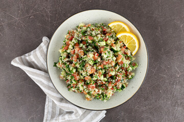 Tabbouleh salad with quinoa, tomatoes, cucumbers, parsley, mint and lemon juice on a brown background. Top view. 