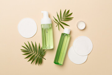 Foaming facial cleanser and micellar water with eco pads on color background, top view