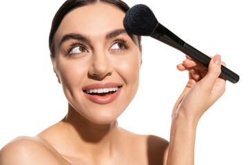 smiling woman with bare shoulders holding soft powder brush near face isolated on white.