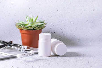 Doctor’s office with laptop, medical stethoscope, two bottles with drugs and succulent flower on white marble table with copy space for your text.