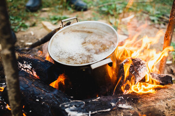 Preparing of cooking in woods outdoor. Brutal Cook soupwith meat or fish in hiking trip. Tourist warms up dinner in campfire. Camp on travel, place for bonfire. Survival in wild adventure in summer