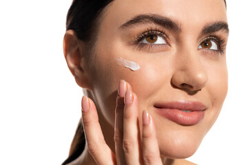 close up view of young woman with face cream on cheek touching face isolated on white.