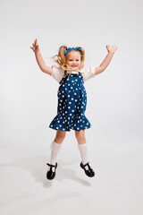 Beautiful cute little girl, child in retro style dress jumping, posing against grey studio background. Concept of childhood, game, emotions, activity, leisure time, retro style, fashion.