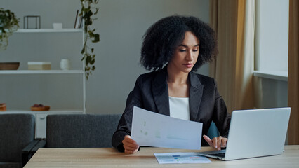 African teacher worker business woman work with graphics documents at home office check documentation enter financial data to laptop processing online information paying bills in computer banking app