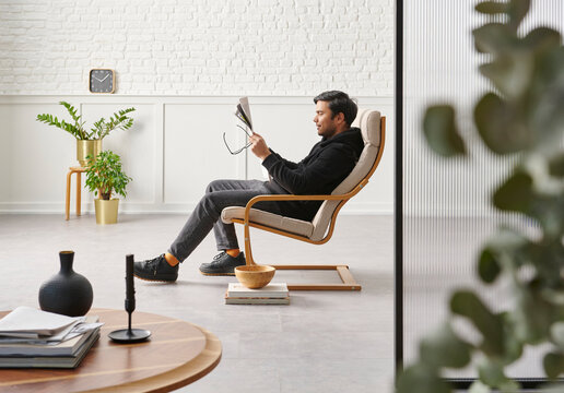 Rocker chair in the white room, man is reading newspaper, brick and classic wall background, chamber, green plant leaf close up blur, working table.