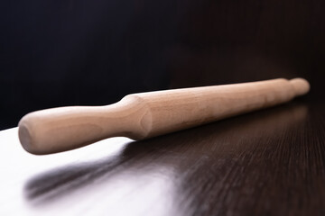 Selective focus. A wooden light rolling pin lies on a dark countertop surface against a black background