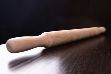 Selective focus. A wooden light rolling pin lies on a dark countertop surface against a black...