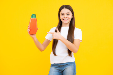 Happy portrait of child teen girl with shampoos conditioners and shower gel. Long hair care of teenager. Presenting cosmetic product, shampoo bottle. Smiling girl.