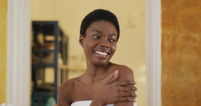 Portrait of smiling african american woman with towel touching her skin in bathroom